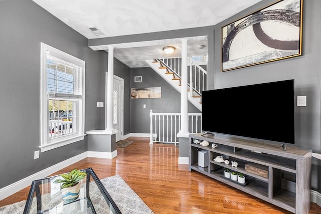 living room with wood finished floors, ornate columns, visible vents, stairway, and baseboards