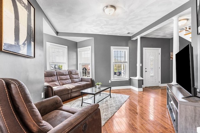 living area featuring light wood-type flooring, visible vents, baseboards, and decorative columns
