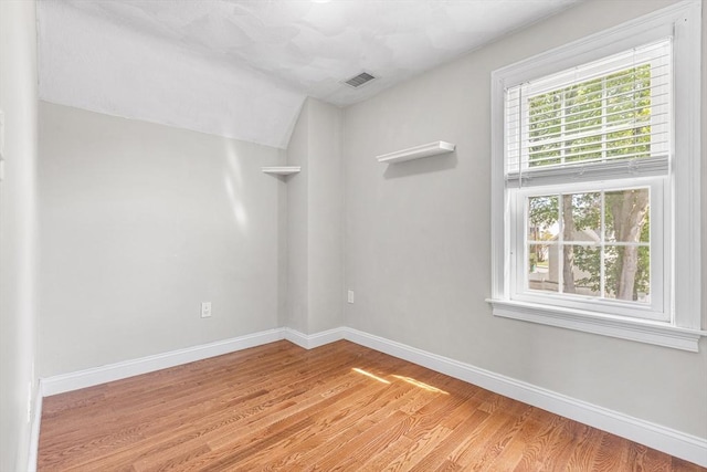 spare room featuring lofted ceiling, baseboards, visible vents, and wood finished floors