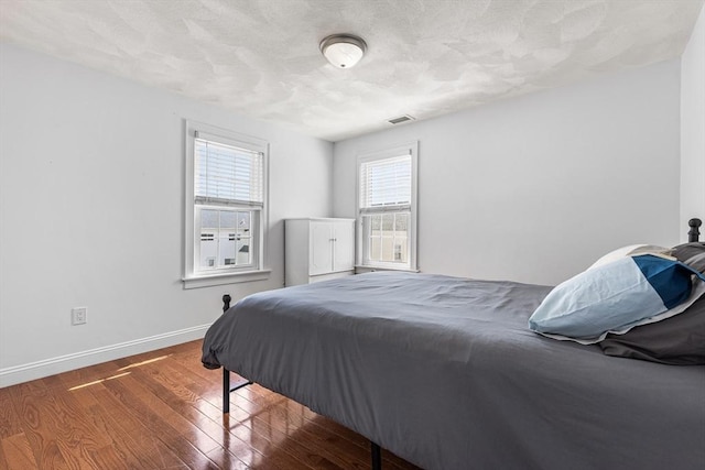 bedroom featuring baseboards, visible vents, a textured ceiling, and wood finished floors