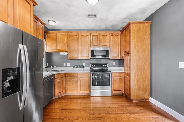 kitchen featuring a sink, appliances with stainless steel finishes, light countertops, baseboards, and light wood-style floors