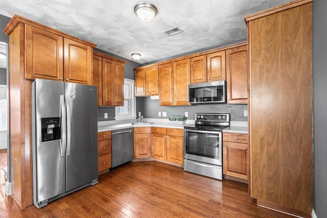 kitchen featuring a sink, stainless steel appliances, dark wood-type flooring, visible vents, and light countertops