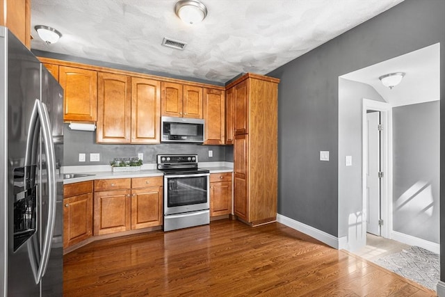 kitchen featuring stainless steel appliances, visible vents, dark wood-style flooring, light countertops, and baseboards