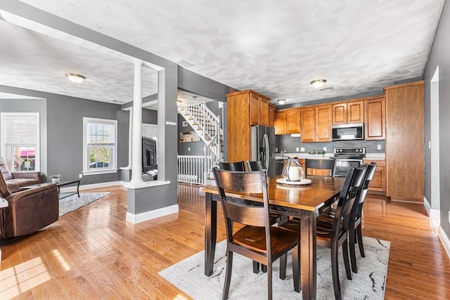 dining space featuring stairway, light wood finished floors, baseboards, and ornate columns