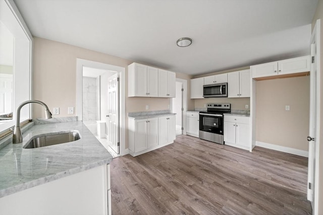 kitchen with appliances with stainless steel finishes, a sink, wood finished floors, white cabinets, and light stone counters