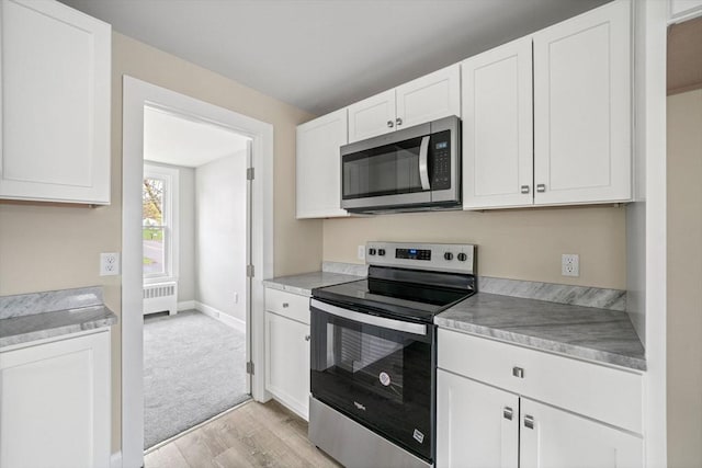 kitchen featuring appliances with stainless steel finishes, radiator, light wood finished floors, white cabinetry, and baseboards