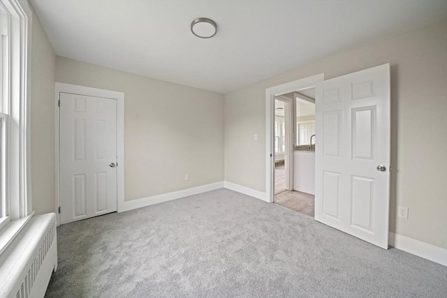 unfurnished bedroom featuring carpet floors, baseboards, and radiator heating unit