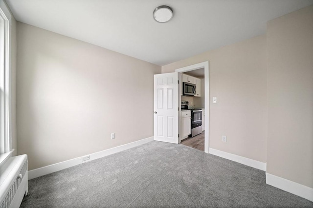 carpeted empty room featuring baseboards and radiator