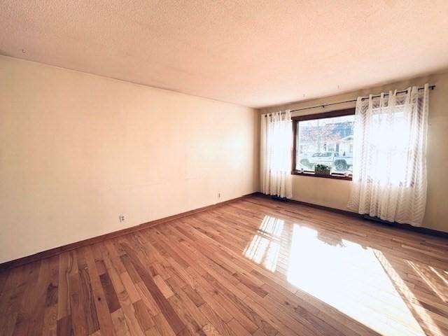 unfurnished room with baseboards, a textured ceiling, and wood finished floors