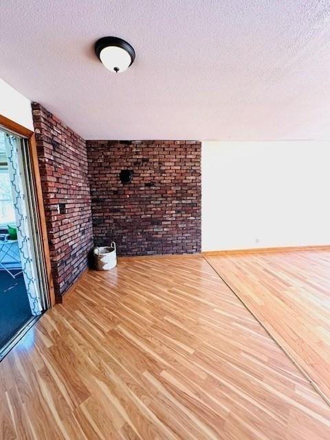 empty room featuring a textured ceiling, brick wall, and wood finished floors