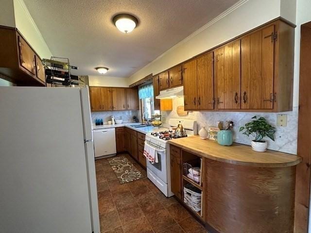 kitchen featuring brown cabinetry, white appliances, a textured ceiling, under cabinet range hood, and a sink