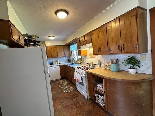 kitchen featuring white appliances, a textured ceiling, under cabinet range hood, brown cabinets, and a sink