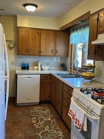 kitchen with tasteful backsplash, brown cabinets, a sink, under cabinet range hood, and white appliances