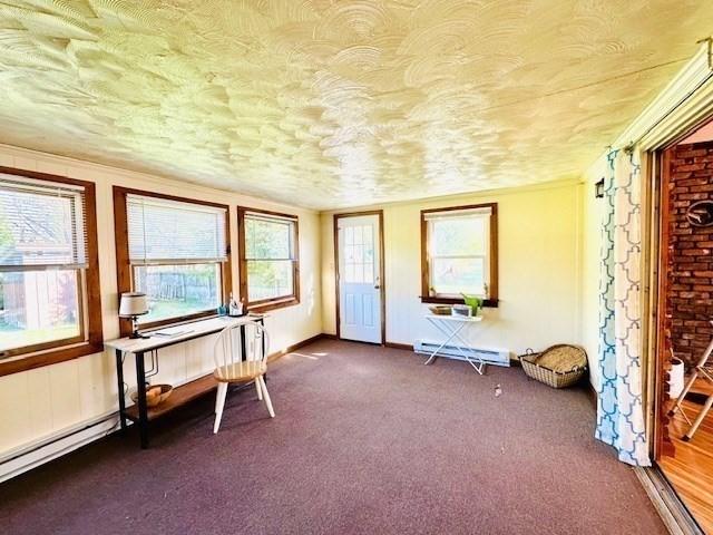 unfurnished room with dark colored carpet, a textured ceiling, a healthy amount of sunlight, and baseboard heating