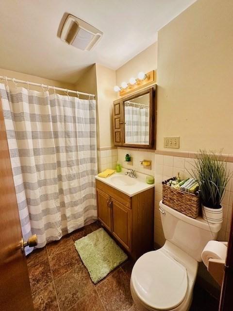 full bath featuring visible vents, tile walls, a wainscoted wall, vanity, and toilet