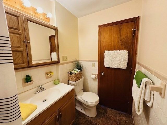 bathroom featuring tile walls, tile patterned flooring, a wainscoted wall, vanity, and toilet