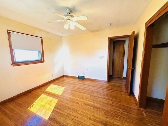 empty room with baseboards, ceiling fan, wood finished floors, and visible vents
