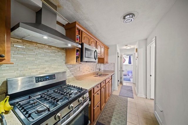 kitchen featuring stainless steel appliances, wall chimney exhaust hood, a sink, tasteful backsplash, and light tile patterned flooring