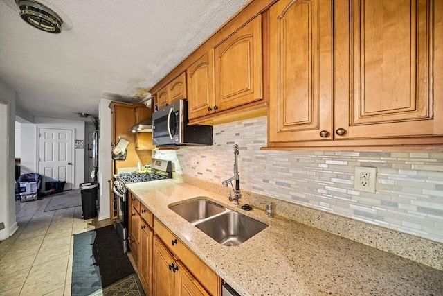 kitchen with appliances with stainless steel finishes, a sink, brown cabinetry, light stone counters, and tasteful backsplash