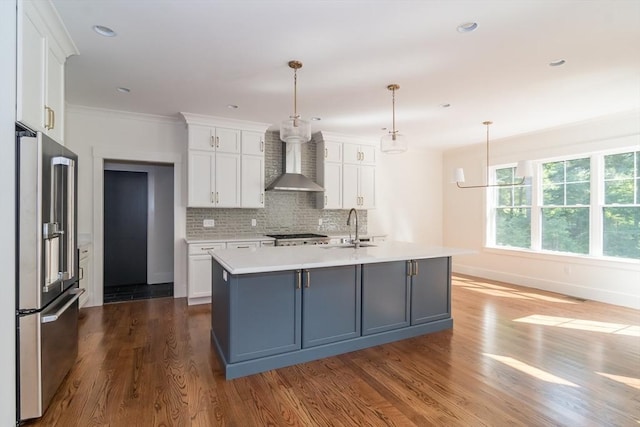 kitchen featuring high end refrigerator, sink, hanging light fixtures, wall chimney exhaust hood, and white cabinetry