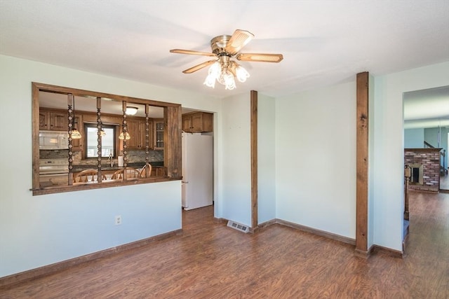 unfurnished living room featuring a sink, visible vents, baseboards, dark wood-type flooring, and ceiling fan