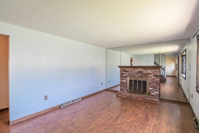 unfurnished living room featuring baseboards, a fireplace, visible vents, and wood finished floors