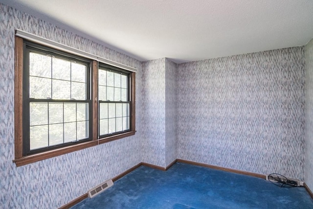 carpeted spare room featuring a textured ceiling, baseboards, visible vents, and wallpapered walls
