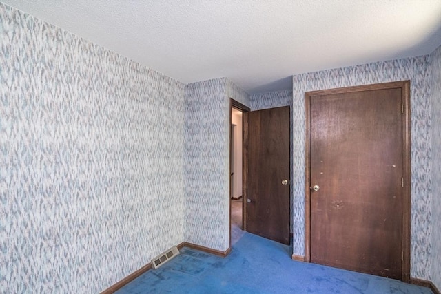 empty room with wallpapered walls, carpet floors, a textured ceiling, visible vents, and baseboards