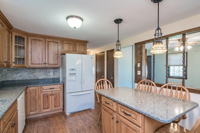 kitchen with tasteful backsplash, white appliances, dark wood finished floors, a kitchen bar, and glass insert cabinets