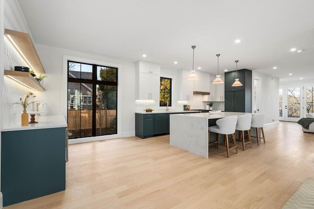 kitchen with white cabinets, light hardwood / wood-style floors, pendant lighting, a breakfast bar, and a center island