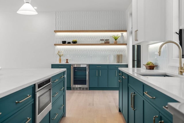 bar with light wood-type flooring, wine cooler, sink, stainless steel microwave, and pendant lighting