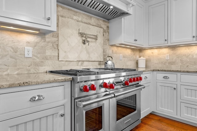 kitchen featuring white cabinetry, light wood-type flooring, backsplash, premium range hood, and luxury stove