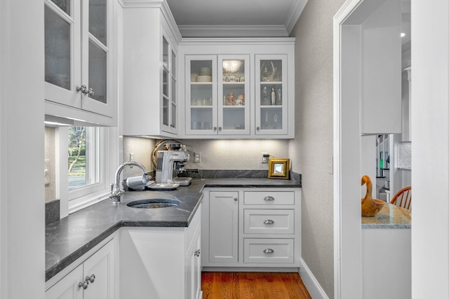 interior space with hardwood / wood-style flooring, white cabinets, ornamental molding, sink, and dark stone countertops