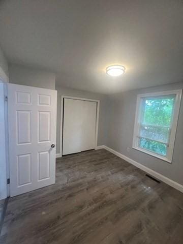 unfurnished bedroom featuring a closet, wood finished floors, visible vents, and baseboards