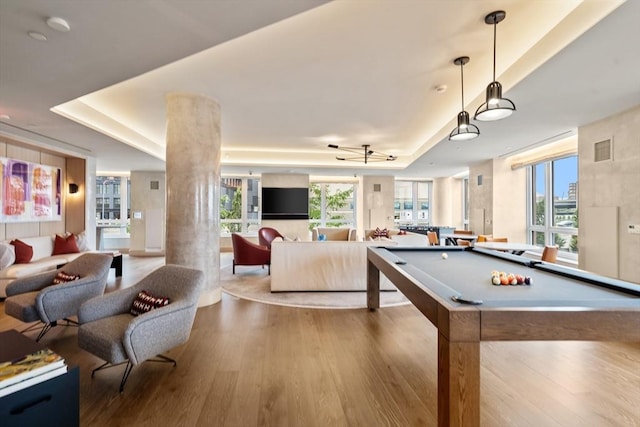 rec room with a wealth of natural light, visible vents, a tray ceiling, and wood finished floors