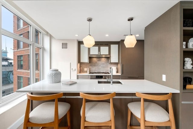 kitchen featuring visible vents, a sink, decorative backsplash, light countertops, and decorative light fixtures