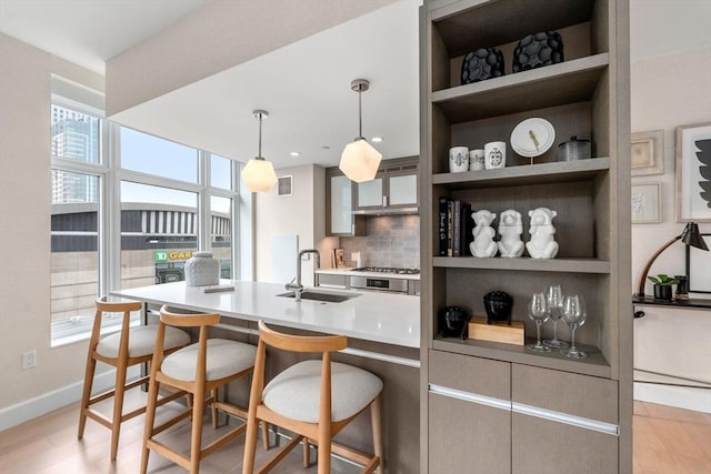 kitchen featuring a sink, pendant lighting, a breakfast bar, stainless steel gas stovetop, and open shelves