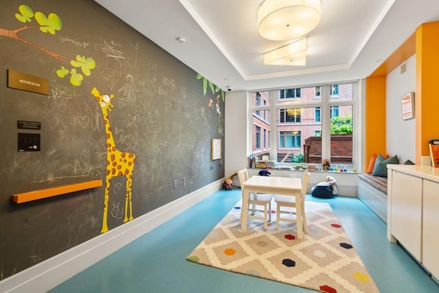 recreation room with visible vents, a tray ceiling, and baseboards