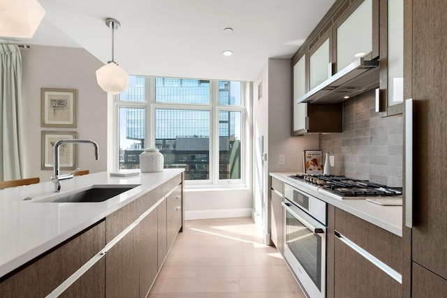 kitchen with light wood finished floors, a sink, light countertops, appliances with stainless steel finishes, and backsplash