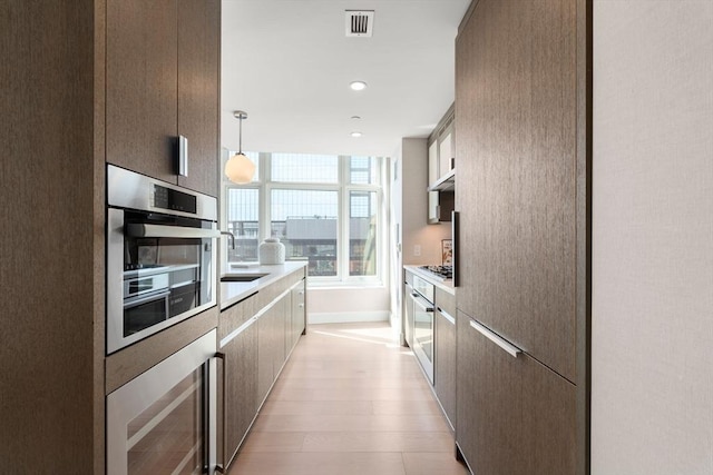 kitchen featuring visible vents, light wood-type flooring, a sink, stainless steel gas stovetop, and light countertops