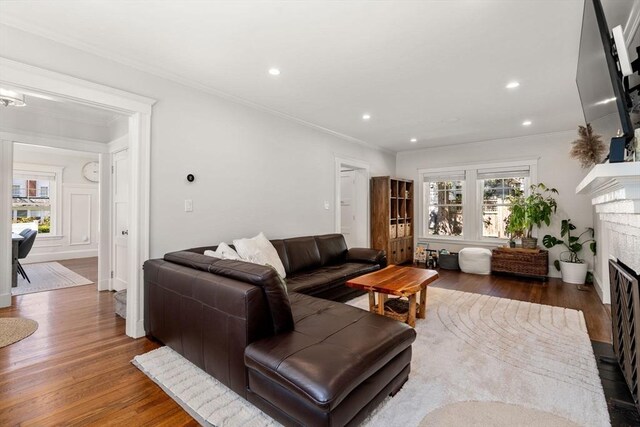 living room with crown molding, recessed lighting, a fireplace with flush hearth, and wood finished floors