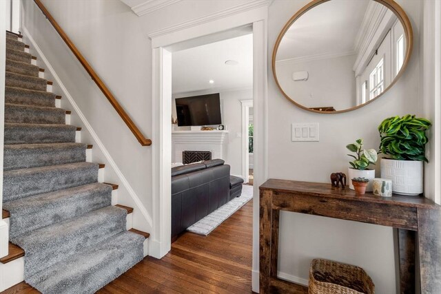 stairs featuring baseboards, ornamental molding, hardwood / wood-style flooring, and a fireplace
