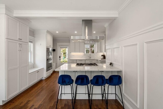 kitchen featuring a breakfast bar area, crown molding, appliances with stainless steel finishes, and island exhaust hood