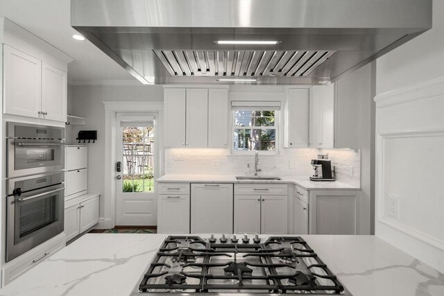 kitchen featuring wall chimney exhaust hood, white cabinets, tasteful backsplash, a sink, and appliances with stainless steel finishes