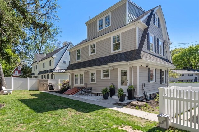 rear view of house featuring roof with shingles, a gambrel roof, a fenced backyard, a lawn, and a patio