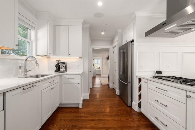 kitchen featuring white cabinets, a sink, wall chimney exhaust hood, stainless steel appliances, and dark wood-style floors