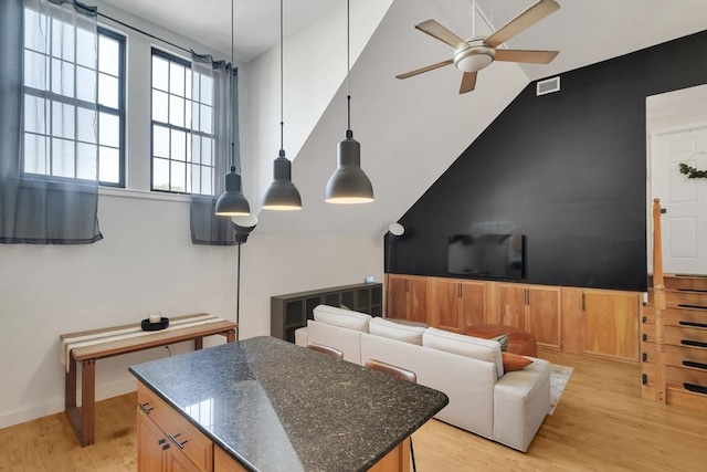 living room featuring visible vents, light wood-style floors, a ceiling fan, and vaulted ceiling