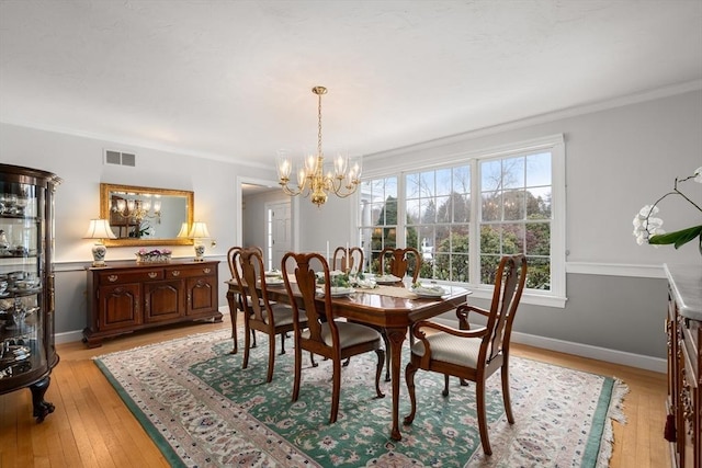 dining area with light wood-style floors, a notable chandelier, visible vents, and crown molding