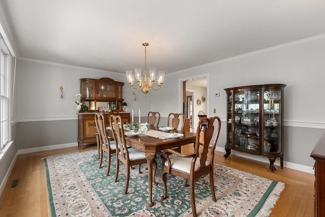 dining room with crown molding, visible vents, a chandelier, light wood-type flooring, and baseboards