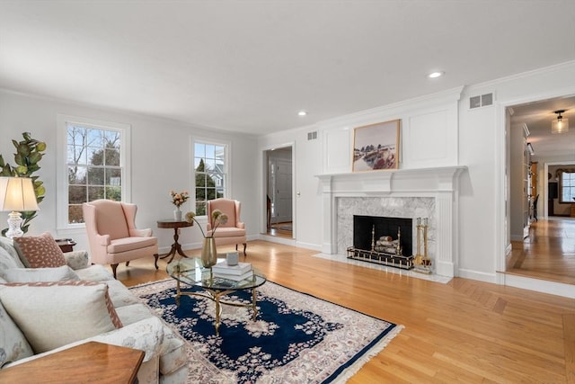 living room featuring light wood-type flooring, visible vents, crown molding, and a high end fireplace